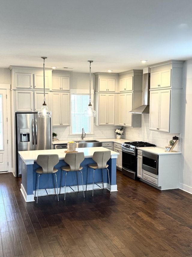 kitchen featuring a kitchen island, a sink, light countertops, wall chimney range hood, and appliances with stainless steel finishes