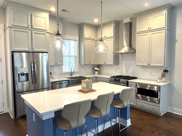 kitchen with wall chimney range hood, appliances with stainless steel finishes, dark wood-type flooring, and a sink