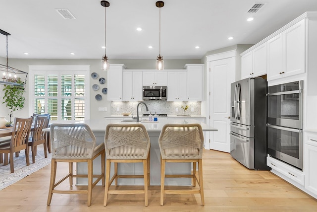 kitchen featuring light hardwood / wood-style floors, stainless steel appliances, decorative light fixtures, and an island with sink