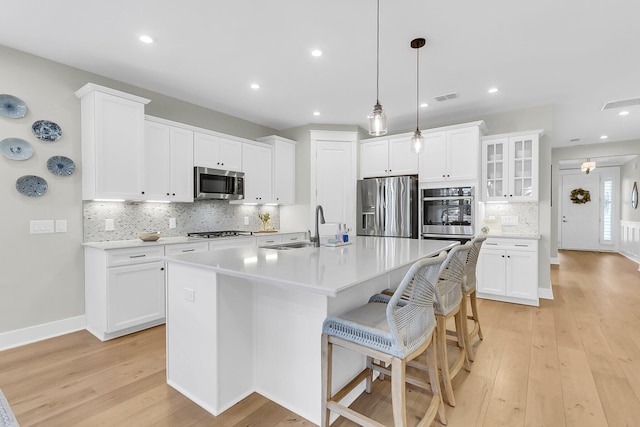 kitchen with stainless steel appliances, light wood-type flooring, an island with sink, and white cabinets