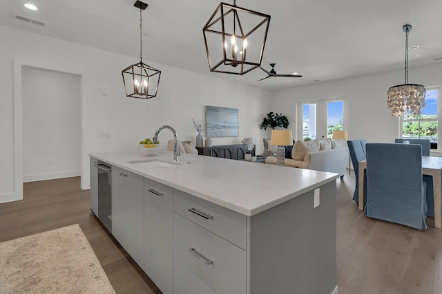 kitchen with pendant lighting, hardwood / wood-style flooring, an island with sink, sink, and a notable chandelier