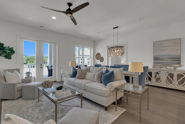 living room featuring a wealth of natural light, wood-type flooring, french doors, and ceiling fan with notable chandelier