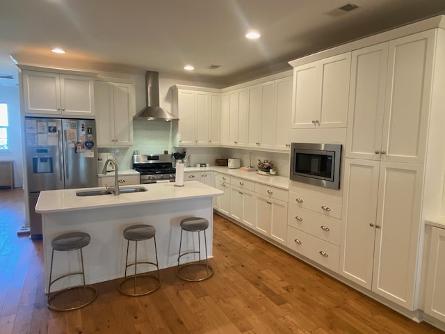 kitchen with stainless steel appliances, visible vents, a sink, wood finished floors, and wall chimney exhaust hood