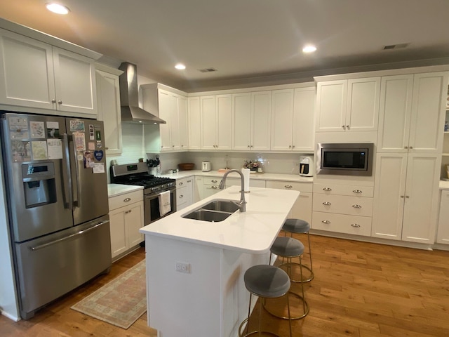 kitchen with light wood finished floors, light countertops, stainless steel appliances, wall chimney range hood, and a sink