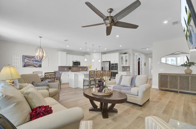 living room with ceiling fan with notable chandelier and light hardwood / wood-style floors