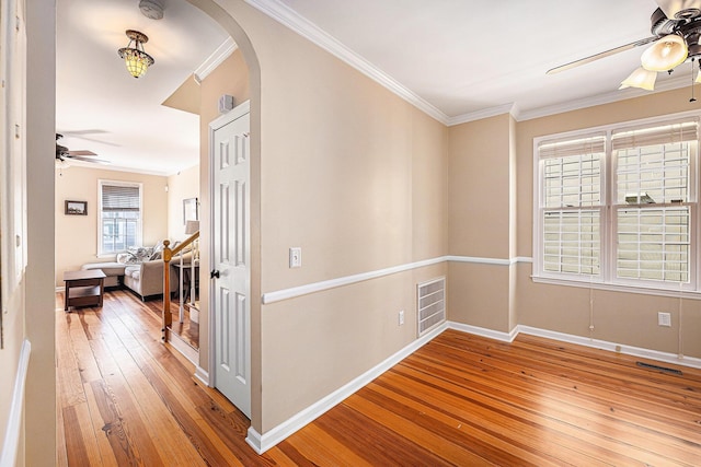 interior space featuring light wood-type flooring, visible vents, arched walkways, crown molding, and ceiling fan