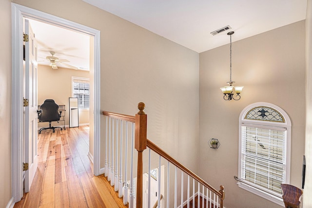 hall featuring visible vents, baseboards, light wood-type flooring, an upstairs landing, and a notable chandelier