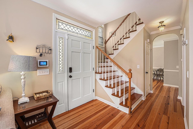 entryway featuring crown molding, baseboards, arched walkways, and light wood-type flooring