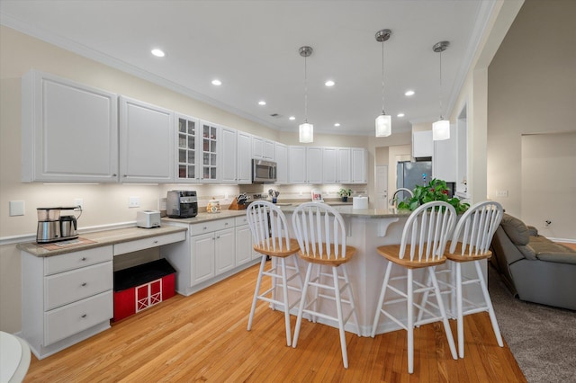 kitchen featuring appliances with stainless steel finishes, crown molding, a breakfast bar, white cabinetry, and light wood-type flooring