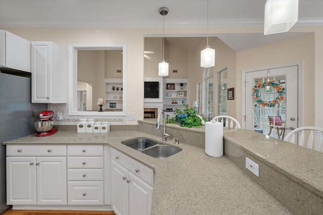 kitchen featuring a sink, white cabinetry, crown molding, hanging light fixtures, and built in features