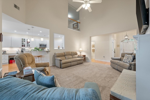 living room with a high ceiling, baseboards, a ceiling fan, and light wood finished floors