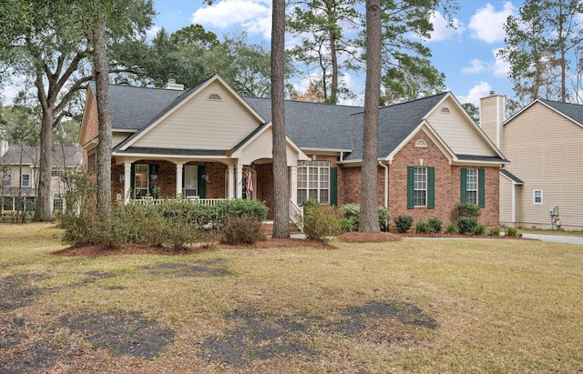 traditional home featuring brick siding, covered porch, a front yard, and roof with shingles