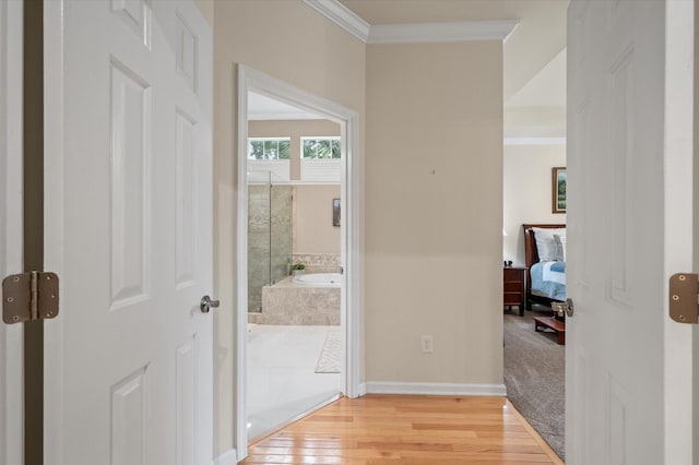corridor featuring light wood-style flooring, ornamental molding, and baseboards