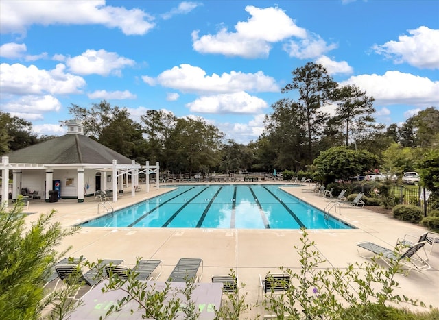 community pool with a patio area, fence, and view of scattered trees