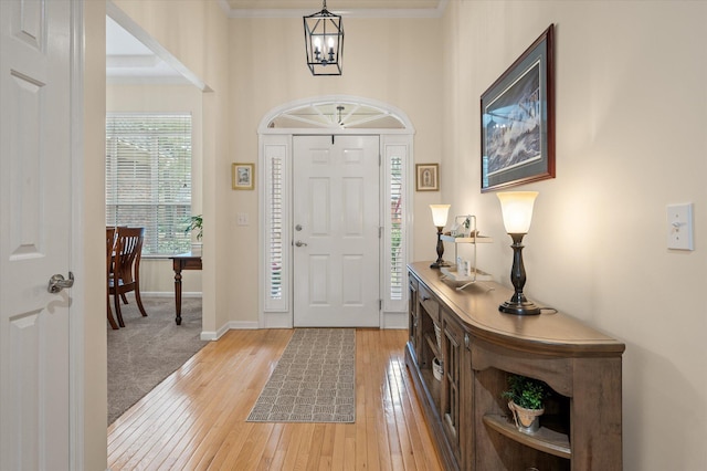 foyer featuring a chandelier, light wood finished floors, baseboards, and ornamental molding