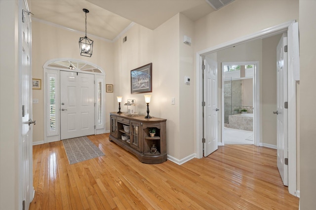 entrance foyer featuring light wood-style floors, baseboards, a towering ceiling, and ornamental molding