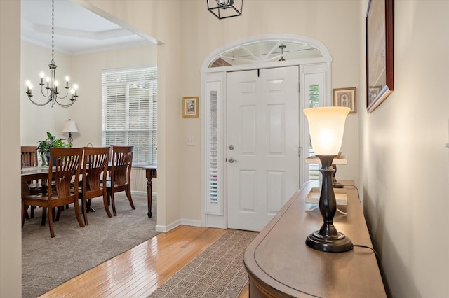 entryway with a chandelier, wood finished floors, crown molding, and baseboards