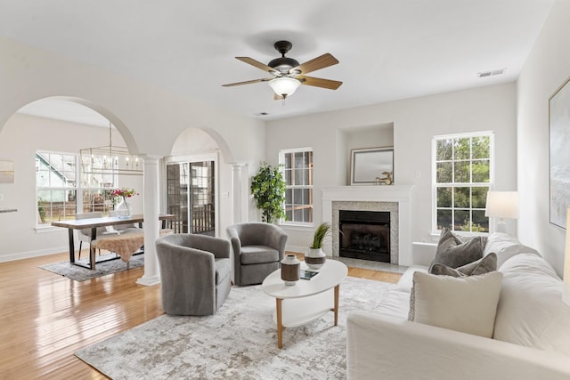 living room featuring a high end fireplace, visible vents, ceiling fan, decorative columns, and wood finished floors