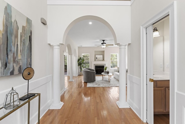 hallway with a sink, decorative columns, arched walkways, and light wood finished floors