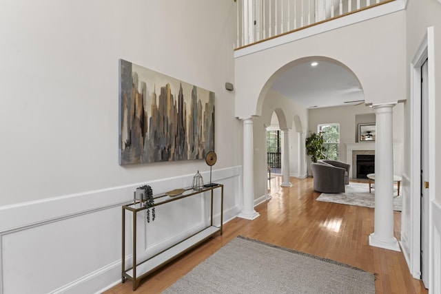 corridor featuring wood finished floors, baseboards, ornate columns, arched walkways, and a towering ceiling