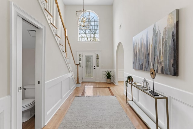 foyer entrance featuring a towering ceiling, light wood-style floors, wainscoting, a decorative wall, and a chandelier