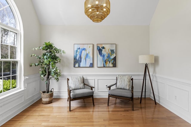 living area featuring lofted ceiling, a notable chandelier, wood finished floors, and wainscoting