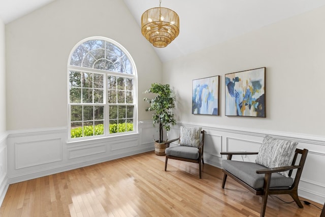 living area with vaulted ceiling, a notable chandelier, a wainscoted wall, and hardwood / wood-style floors