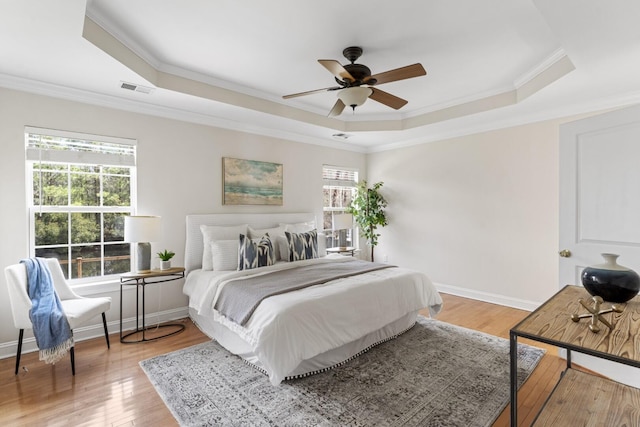 bedroom with visible vents, baseboards, a tray ceiling, ornamental molding, and light wood-style flooring