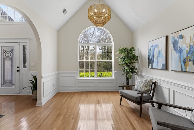 living area featuring visible vents, light wood-style flooring, arched walkways, a chandelier, and vaulted ceiling