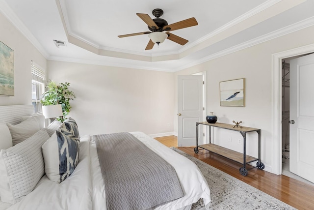 bedroom with wood finished floors, visible vents, baseboards, a tray ceiling, and crown molding