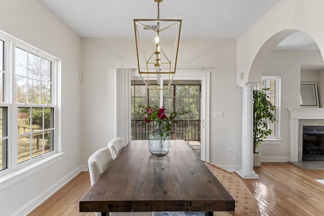 dining area with a high end fireplace, baseboards, a chandelier, wood finished floors, and arched walkways