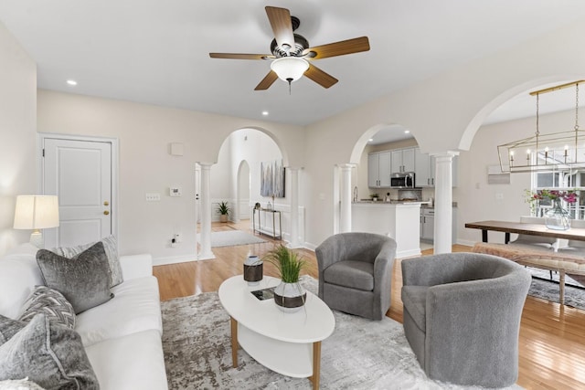 living area with ceiling fan with notable chandelier, arched walkways, ornate columns, and light wood-type flooring