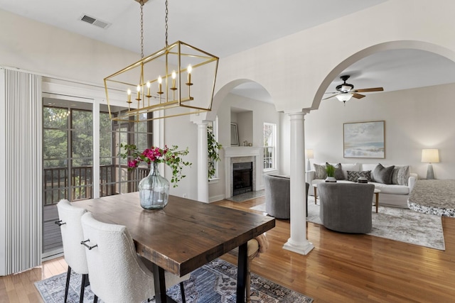 dining room with visible vents, ceiling fan, a fireplace with flush hearth, decorative columns, and wood finished floors