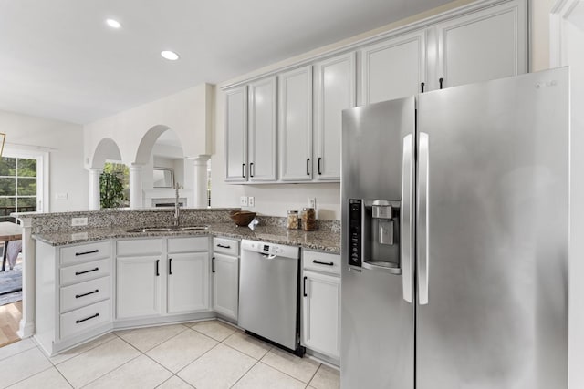 kitchen with light tile patterned floors, appliances with stainless steel finishes, a peninsula, stone countertops, and a sink