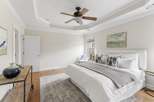 bedroom with visible vents, crown molding, baseboards, light wood-type flooring, and a tray ceiling