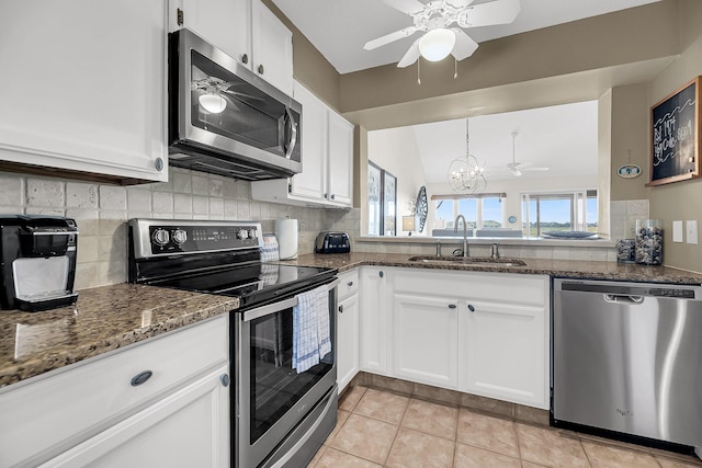 kitchen featuring stainless steel appliances, dark stone counters, sink, light tile patterned floors, and white cabinetry