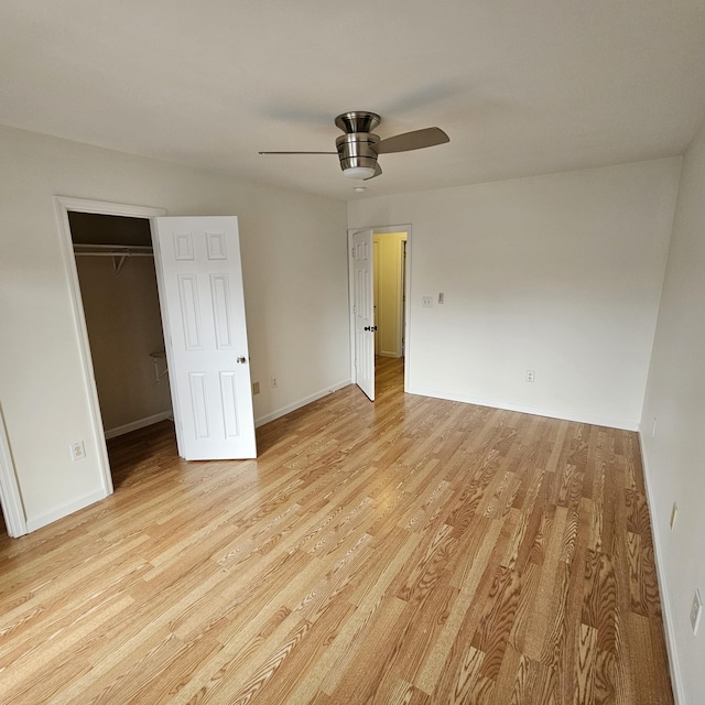 unfurnished bedroom with ceiling fan, a spacious closet, a closet, and light wood-type flooring