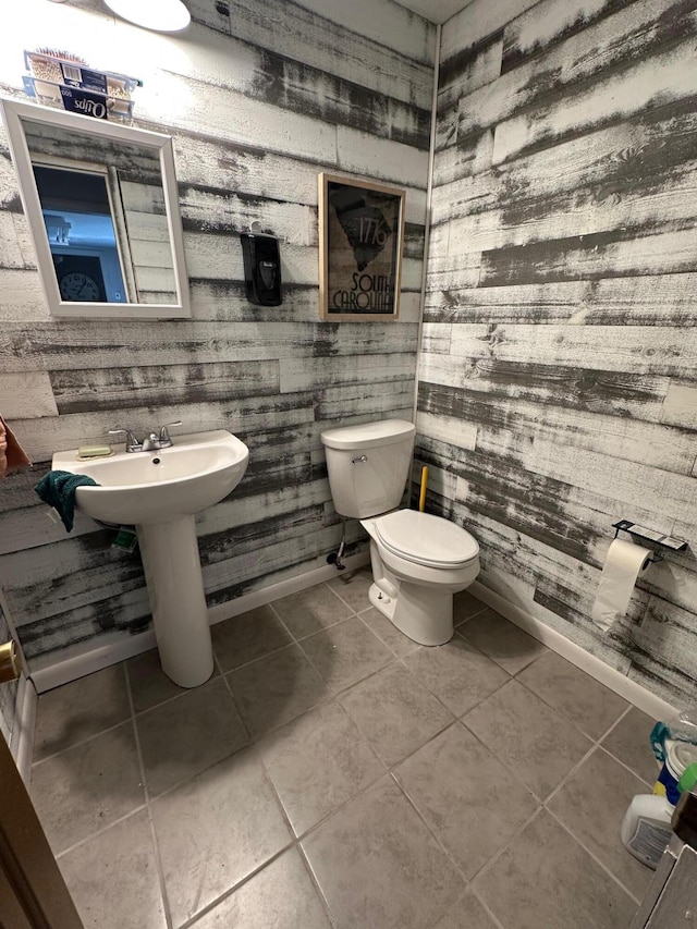 half bathroom with tile patterned floors, baseboards, toilet, and a sink