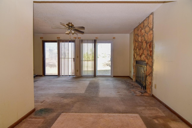 unfurnished living room featuring ceiling fan, a stone fireplace, carpet floors, and a textured ceiling