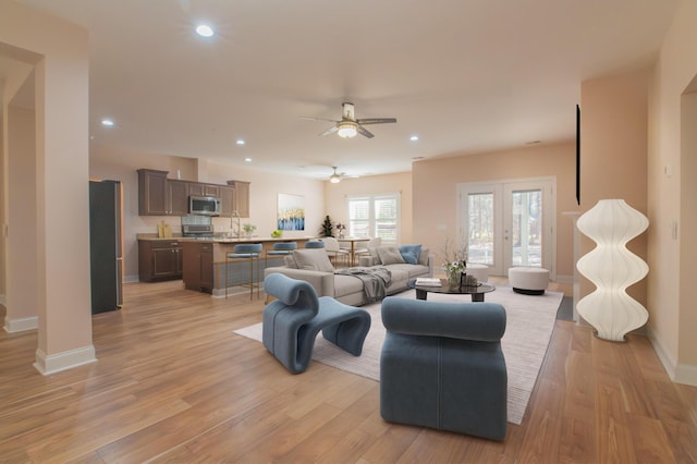 living room featuring ceiling fan, light hardwood / wood-style flooring, french doors, and sink