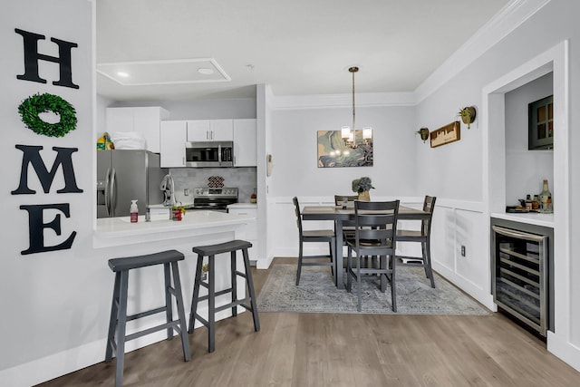 dining room featuring a notable chandelier, crown molding, light hardwood / wood-style floors, sink, and wine cooler