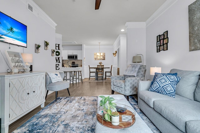 living room with wood-type flooring, ornamental molding, and an inviting chandelier