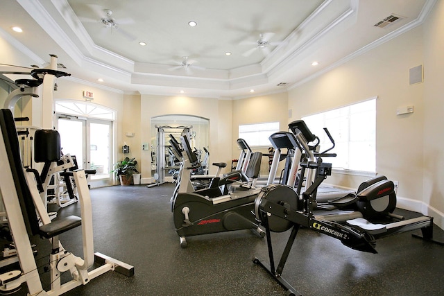 gym with ceiling fan, a wealth of natural light, ornamental molding, and a tray ceiling