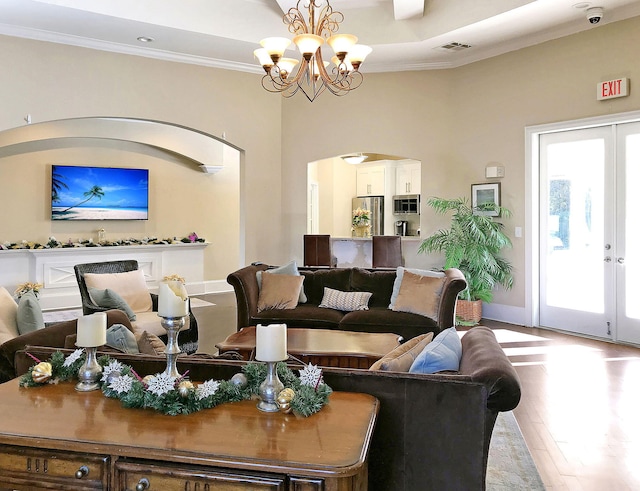 living room featuring crown molding, french doors, a tray ceiling, light hardwood / wood-style floors, and an inviting chandelier