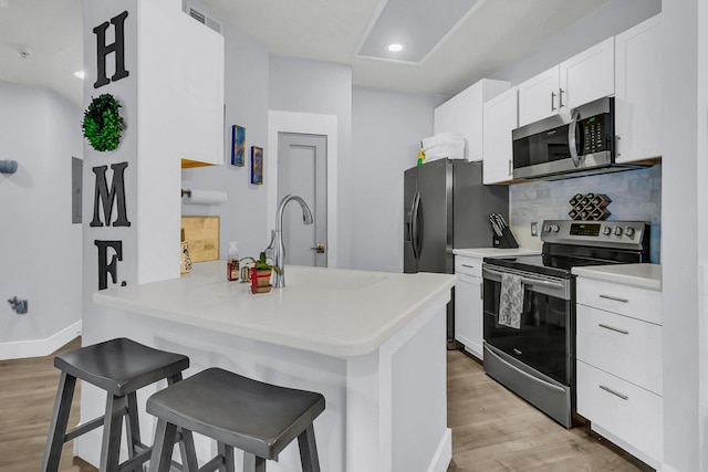 kitchen with white cabinets, stainless steel appliances, a kitchen bar, and kitchen peninsula