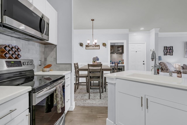 kitchen with decorative backsplash, white cabinets, decorative light fixtures, sink, and stainless steel appliances