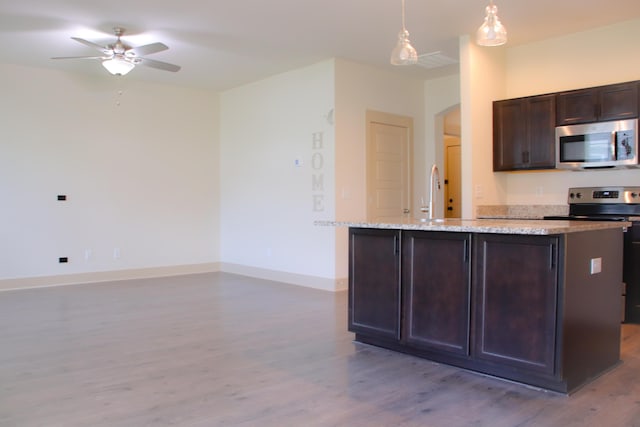 303 Citation Way, Moncks Corner, SC 29461 - kitchen featuring stainless steel microwave, light wood-style floors, ceiling fan, arched walkways, and a center island with sink