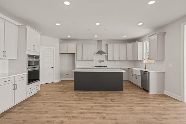 kitchen featuring light wood finished floors, stainless steel appliances, light countertops, a sink, and wall chimney range hood