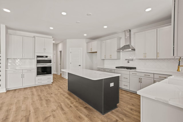 kitchen featuring tasteful backsplash, light wood-style floors, stainless steel double oven, wall chimney range hood, and recessed lighting