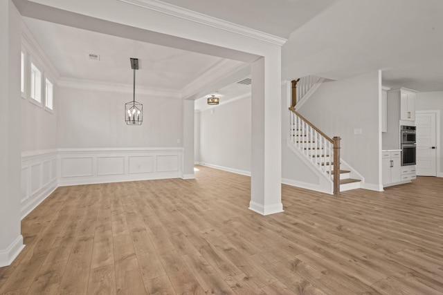 unfurnished dining area featuring stairs, crown molding, wainscoting, and light wood-style floors